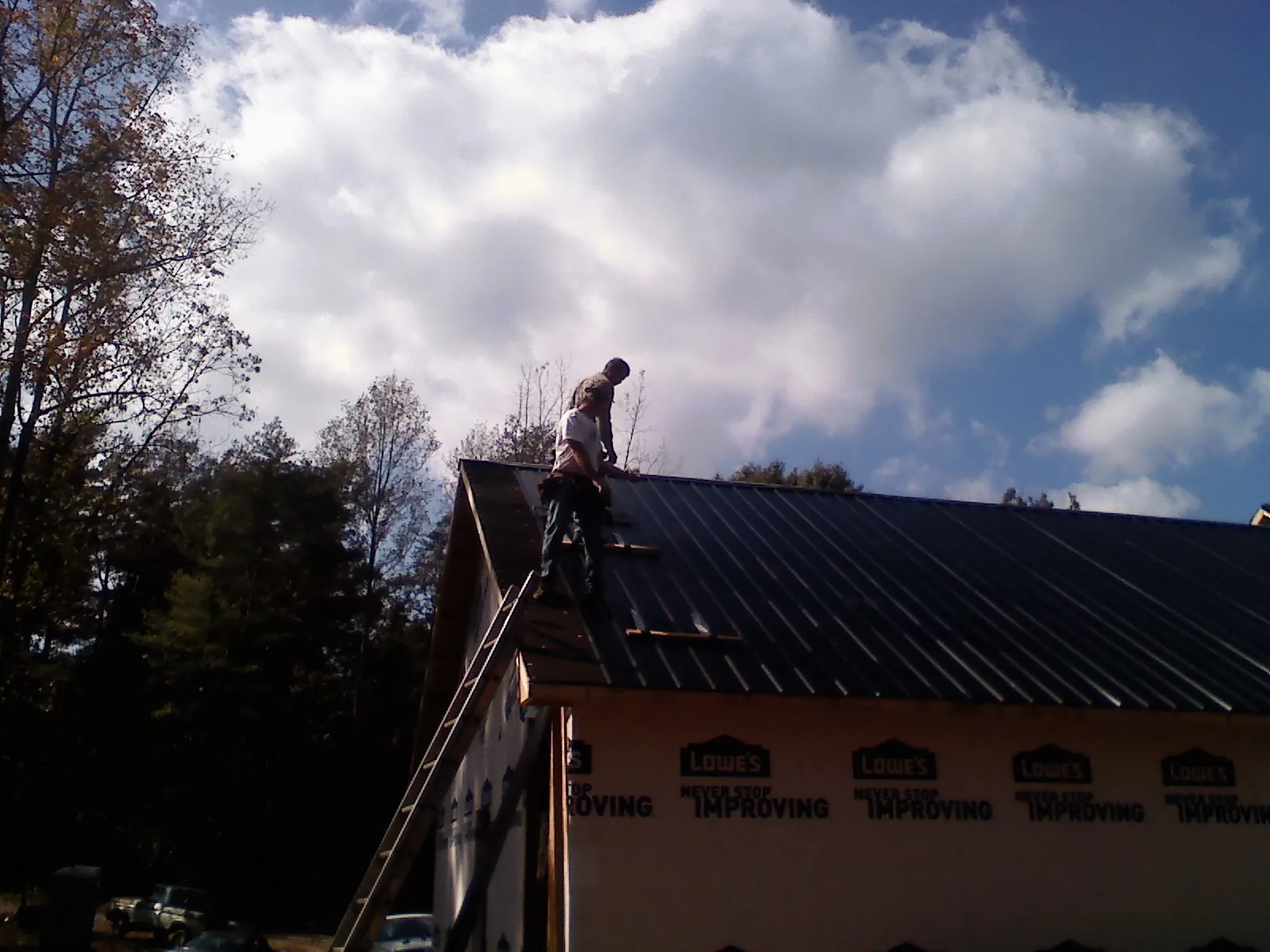 Roofer fastening dark metal panels high against a cloudy sky, from a Roof Inspection job in Edgerton