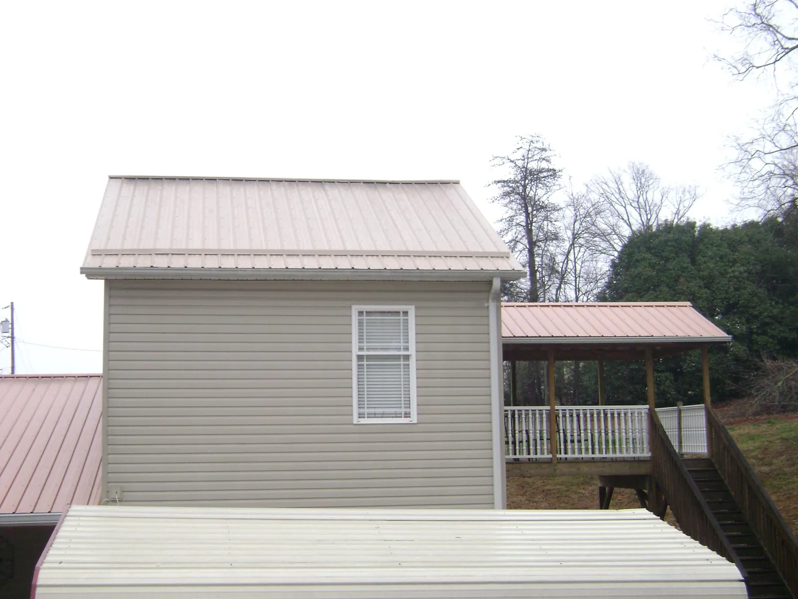 Tan metal roofs on a two story addition and attached porch, from a Roof Replacement job in Edgerton